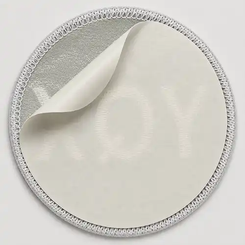Back view of a custom round embroidered patch with a peel-and-stick adhesive backing and partially removed release paper.