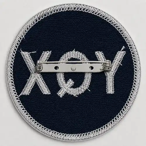 Back view of a custom round embroidered patch with a metal safety pin backing for removable attachment.