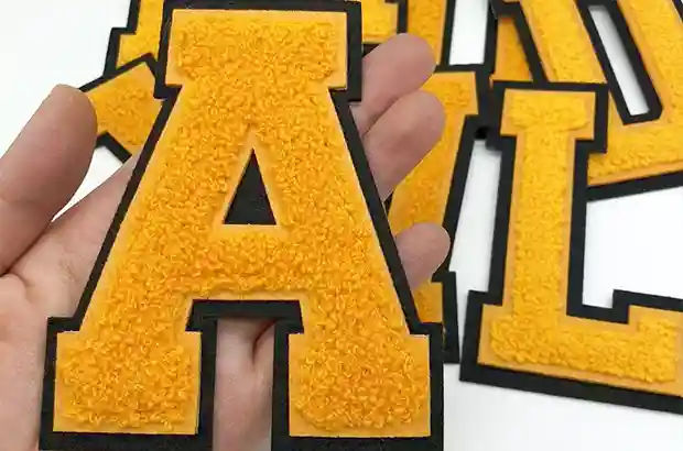 Close-up of a custom varsity-style letter A patch with yellow chenille embroidery and a black felt border.