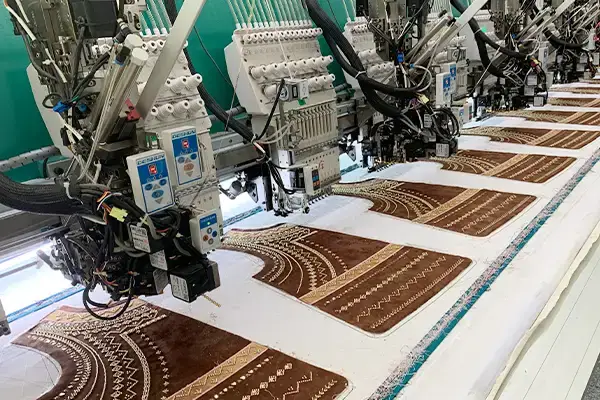 Multi-head embroidery machines stitching decorative brown fabric panels with repeated patterns for bulk production.