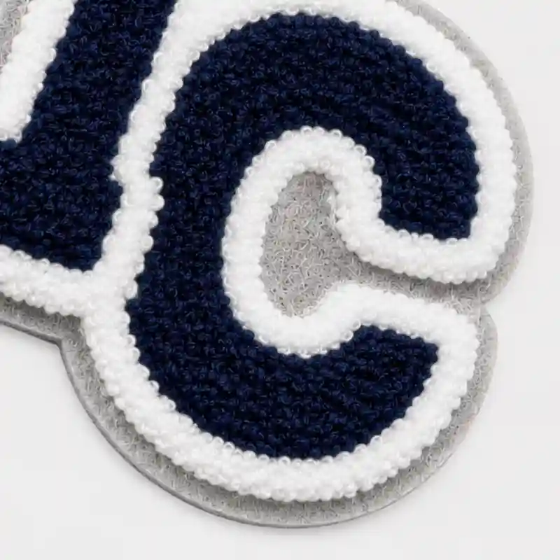Close-up of a chenille patch with navy and white lettering and a layered double felt edge in light gray and white