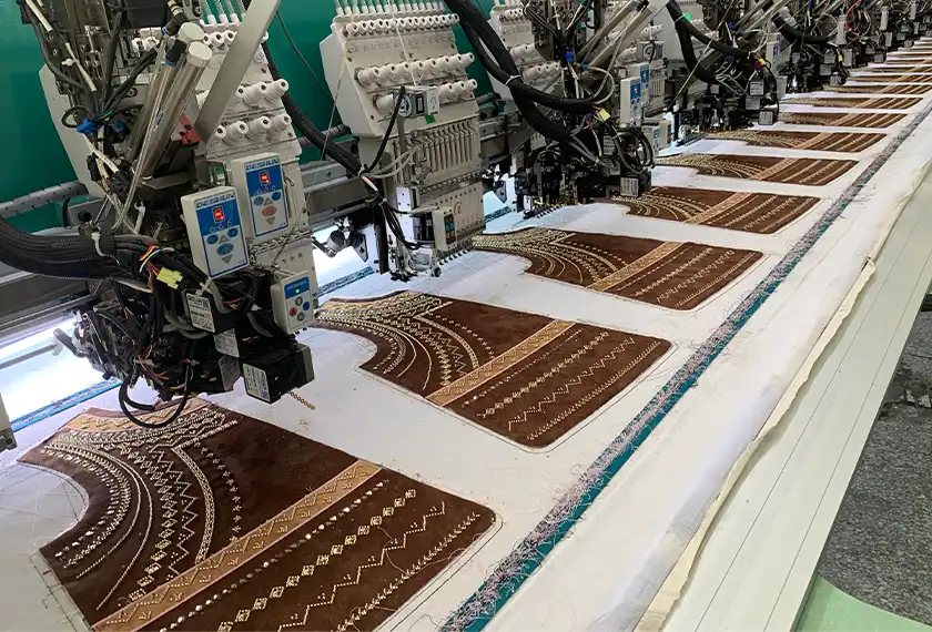 Multi-head industrial embroidery machines stitching decorative patterns on brown garment panels during bulk production.
