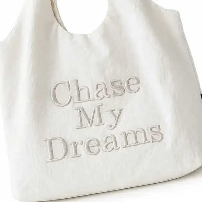 White handbag featuring 3D raised embroidery text on the front panel for textured custom handbag decoration.