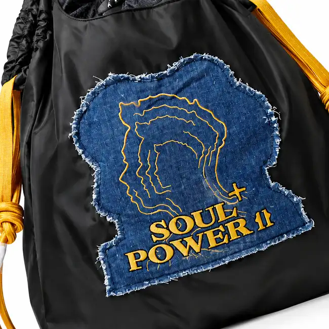 Black handbag featuring a blue denim appliqué with yellow embroidered outlines and lettering on the front panel.