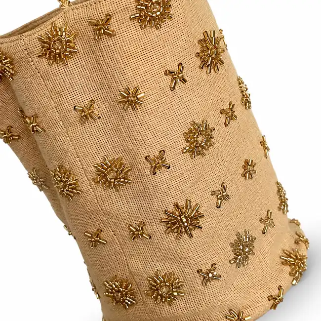 Gold beaded embroidery with floral and starburst motifs decorating a beige textured handbag panel.