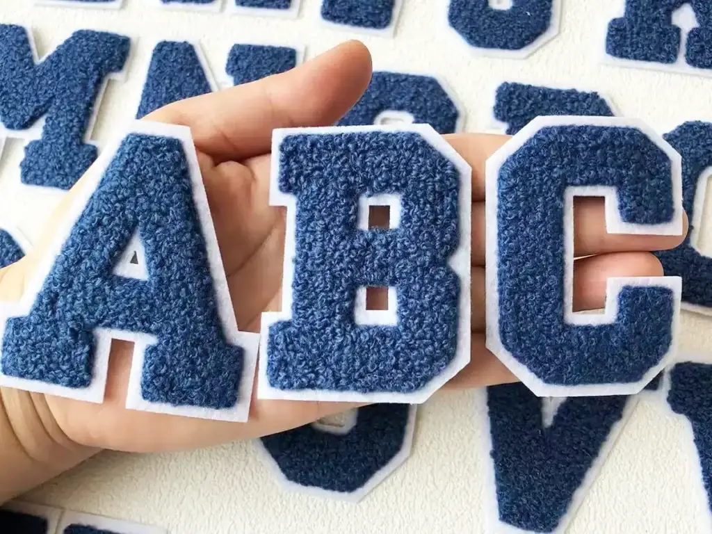 Close-up of blue chenille letter patches showing the thick, soft, raised texture used for varsity-style designs.