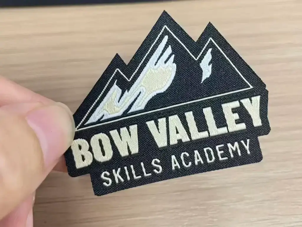 Close-up of a custom woven patch showing fine lettering, clean lines, and detailed mountain artwork on a flat woven surface.