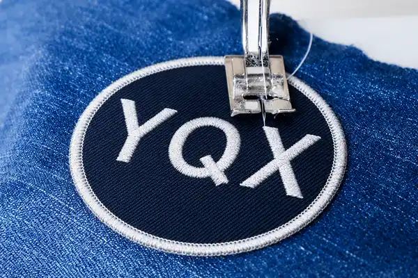 Close-up of a sewing machine stitching a round embroidered patch onto blue denim fabric