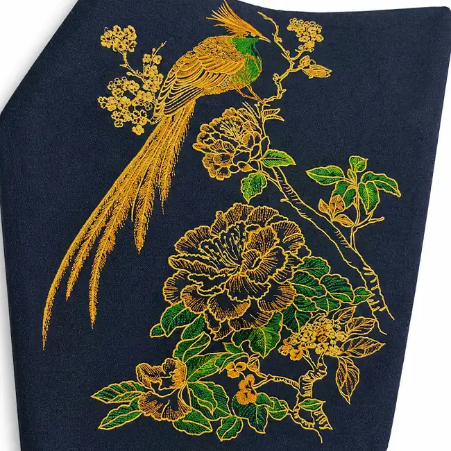 High-precision metallic thread embroidery featuring a detailed bird, flowers, and foliage on a dark fashion garment panel.