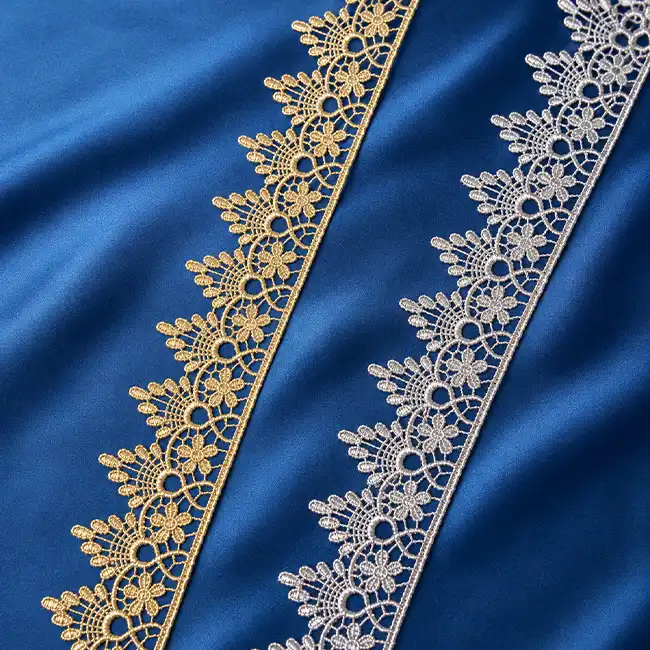 Delicate lace embroidery trim in gold and silver stitched on blue fabric for high-precision fashion garment panel decoration.