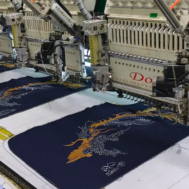Multi-head industrial embroidery machines stitching detailed gold and white decorative patterns on dark blue fashion garment panels.