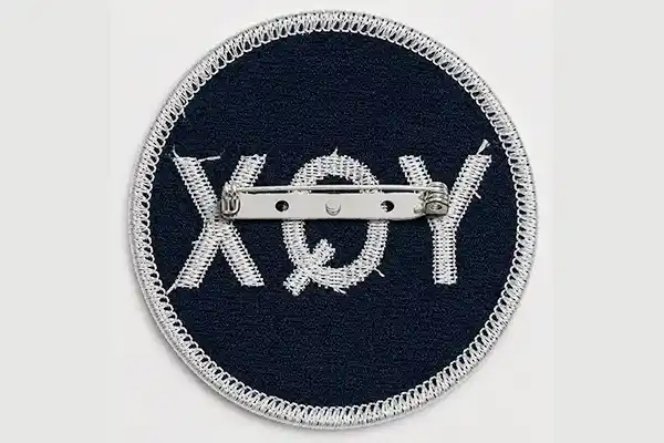 Close-up of a custom embroidered patch with safety pin backing, showing the detachable attachment method for badges, events, uniforms, and temporary applications.