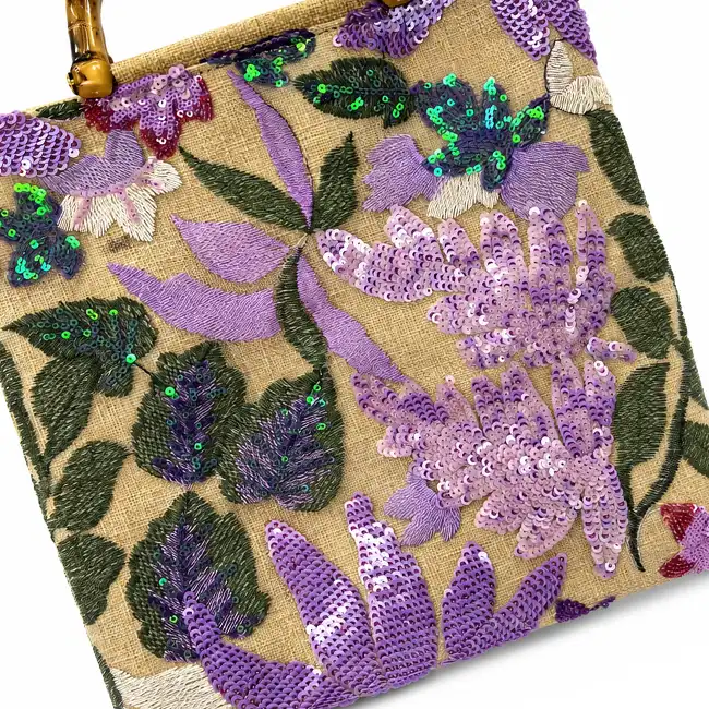 Floral sequin embroidery with purple flowers, green leaves, and shimmering details decorating a textured handbag panel.