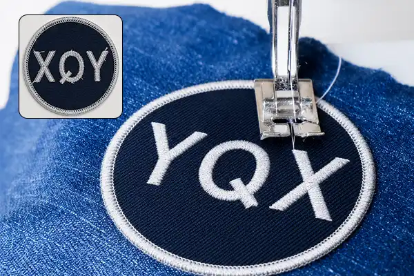 Close-up of a custom embroidered patch being sewn onto denim fabric, showing the stitching process and detailed embroidery quality for garment application.
