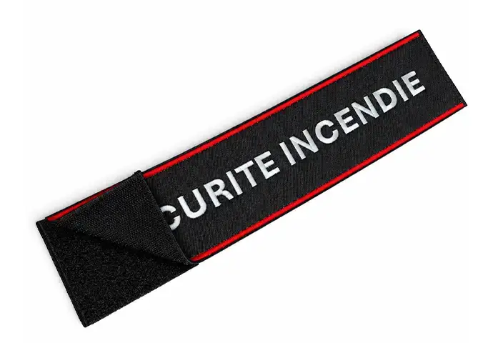 Black custom embroidered hook and loop strap patch with red border, white lettering, and detailed hook-and-loop texture.